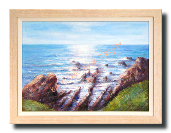 A cliff top view across Hartland Rocks and the sun bathed blue ocean on a calm summer afternoon.